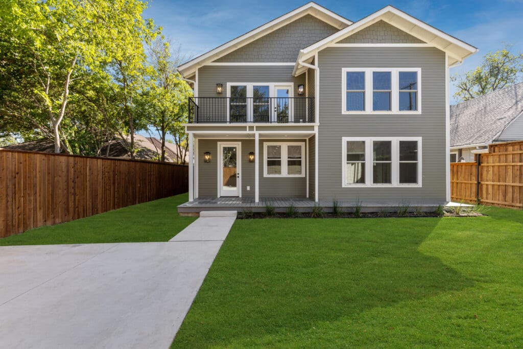 New luxury home with gray hues, white trims, and a serene green backdrop, showcasing modern design and nature's beauty.
